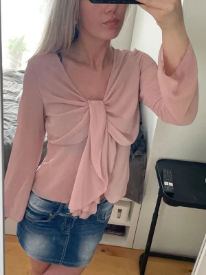 Ljusrosa blus med knyt framtill - Trendig ljusrosa blus i ett tunt, lätt och transparent tyg. Blusen har långa ärmar och en snygg knytning framtill. Perfekt till jeans eller kjol.