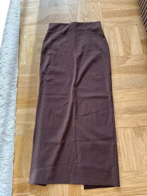 Brun långkjol med slits - Snygg brun långkjol i rak modell med hög midja och slits baktill. Kjolen är enkel och stilren, perfekt att matcha med olika toppar. Materialet känns mjukt och har en lätt stretch och formas längst kroppen. 