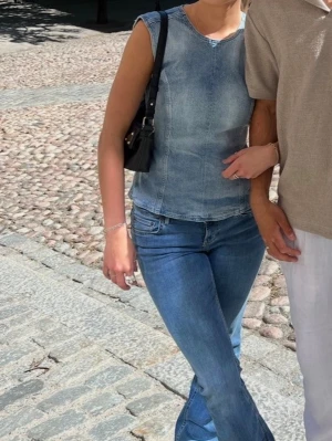 Blå ärmlös linnetopp i denimlook - Snygg ärmlös topp i ljusblå denim med öppen rygg och knyt bak. Toppen har rund halsringning och en croppad passform som ger en trendig look. 