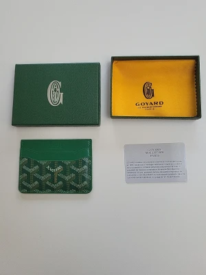 Grön korthållare - Snygg grön korthållare från G0Y4DR med klassiskt mönster och vit logga framtill. Tillverkad i läder och canvas, har flera kortfack och levereras med originalask och certifikat. Perfekt för dig som vill ha något exklusivt och stilrent i fickan.