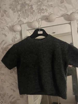 Mörkgrå stickad topp Gina Tricot - Mysig mörkgrå stickad topp från Gina Tricot med korta ärmar och rund hals. Perfekt för lager-på-lager och passar till både jeans och kjol. Enkel och stilren design som är lätt att matcha.