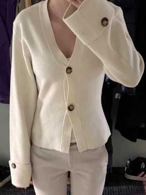 Vit kofta med knappar - Knitted sculptured cardigan i storlek S från Gina Tricot. Använd ett fåtal gånger och är i jättefint skick förutom en tråd som sticker ut (se bild 3) men inget som syns när man har på sig den. Priset kan diskuteras!