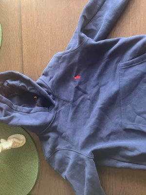 Marinblå hoodie från Polo Ralph Lauren - Snygg marinblå hoodie från Polo Ralph Lauren i slim fit-modell. Klassisk design med huva, känguruficka och röd broderad logga på bröstet. Perfekt för en avslappnad och stilren look.