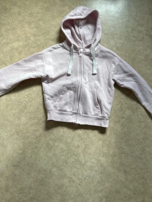 Ljusrosa hoodie med dragkedja - Ljusrosa hoodie med dragkedja framtill och vita snören i huvan. Mjuk insida och två stora fickor på magen. Perfekt för en chill och avslappnad stil. Materialet känns som bomullsmix.