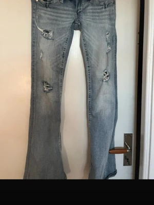 Ljusblå  bootcut jeans - Säljer ett par ljusblå jeans med slitningar och hål på benen. Modellen är bootcut med lätt utsvängda ben och klassisk femficksdesign. Jeansen har en avslappnad vibe och är perfekta för dig som gillar en trendig, casual stil.
