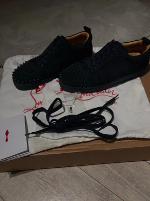 Svarta Christian Louboutin sneakers - Säljer ett par riktigt fräscha navy blue sneakers från Christian Louboutin med ikoniska röda sulor och matt blåa nitar på tån. Riktigt sköna skor (aftermarket) med lite unikt annorlunda design och är nästan som nya då inte mycket användning gjorts pga av strlk. Perfekta för dig som vill sticka ut med en lite mer lyxig stil. Allt medföljs, bag, extra nitar, snören mm. Hör av vid intresse😁