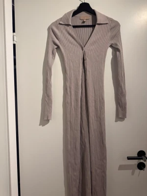 Beige ribbad långklänning med krage - Snygg beige långklänning med ribbad struktur och klassisk krage. Klänningen har lång ärm och figurnära passform, perfekt för dig som gillar stilrena och trendiga plagg. Enkel att styla med sneakers eller boots.