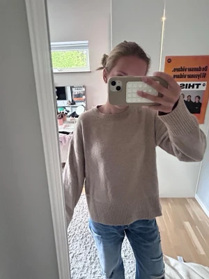 Beige stickad tröja - Mysig beige stickad tröja med rund hals och breda ribbade muddar vid ärmslut och nederkant. Tröjan har en avslappnad,lite  oversized passform och är perfekt att bära till jeans. 