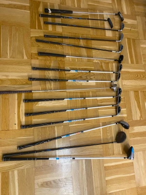 Golfklubbor set med drivers och järn - Säljer ett komplett set golfklubbor med flera järn, drivers och putters. Klubborna har svarta och silverfärgade skaft med svarta grepp och blå detaljer på vissa klubbor. Perfekt för dig som vill börja spela golf eller uppgradera din utrustning.