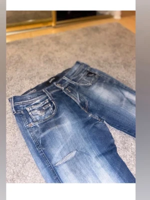 Blå replay jeans med slitningar - Snygga blå replay jeans med slitningar och ljusa tvättade partier. Klassisk femficksmodell och dragkedja. Perfekta för en avslappnad och trendig look.