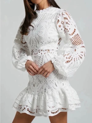 Vit spetsklänning med volang - Superfin vit kort klänning med broderad spets, volang nertill och långa puffärmar. Hög hals och genombrutet mönster ger en romantisk vibe. Perfekt för dig som vill sticka ut med en elegant look.