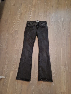 Gråa jeans - Säljer ett par gråa bootcut jeans med fem fickor. Jeansen har dekorativa sömmar och bakfickor med lock och knappar. Perfekta för dig som gillar en klassisk men ändå trendig look. Använda men inte några fläckar eller andra "skador" på jeansen.