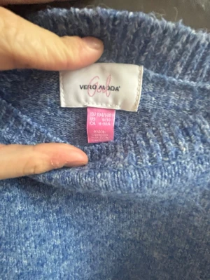 Ljusblå stickad tröja Vero Moda - Mysig ljusblå stickad tröja från Vero Moda med rund halsringning och ribbade muddar vid ärmslut och nederkant. Tröjan har en avslappnad passform och är perfekt för kyliga dagar. Materialet känns mjukt och behagligt mot huden.