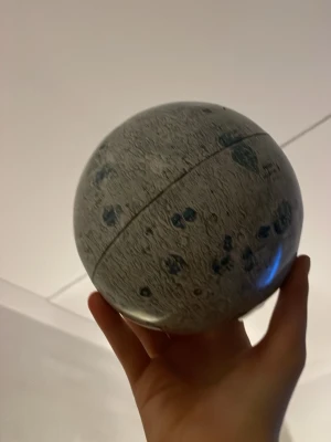 En miniatyr av månen - Säljer en rund ask formad som en måne med detaljerad yta och blågrå kratrar. Asken är gjord av plast från ch är perfekt som dekoration i rummet.