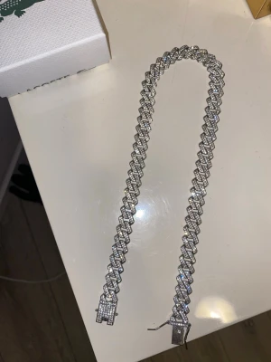 Silverfärgat cuban chain halsband - Säljer ett glittrande halsband i cuban chain-stil med tätt satta stenar som ger en riktigt lyxig känsla. Halsbandet är silverfärgat och har en rejäl låsning framtill. Perfekt för dig som vill sticka ut med accessoarer som syns. Oanvänd