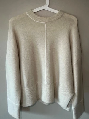 Beige stickad tröja från Zara - Mysig beige stickad tröja från Zara. Tröjan har fina vita detaljer och en avslappnad passform. Myscket bekväm och i väldigt bra skick. 