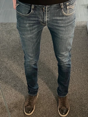 Blå Replay anbass slim fit jeans med slitningar - Säljer ett par blå slim fit jeans med snygga slitningar och tvättade detaljer. Klassisk femficksmodell med normalhög midja och smal passform hela vägen ner. Jeansen har en modern look och passar perfekt till sneakers eller boots. Materialet är mjukt och stretchigt för extra komfort. W30 L32