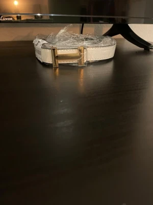 Vitt bälte med guldspänne - Stilrent vitt bälte med ett fyrkantigt guldspänne som ger en lyxig touch till din outfit. Bältet har en slät yta och klassisk design som passar till många olika looks. Perfekt accessoar.