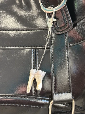 Nyckelring med tandhänge - Unik nyckelring med ett tandformat hänge i benvit färg. Hänget sitter fast i en silverfärgad kedja och karbinhake, perfekt att fästa på väska eller nycklar för en edgy och personlig stil.