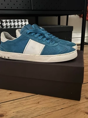  Valentino flycrew - Snygga blåa sneakers från Valentino i mocka med vita detaljer och vita sulor. Skorna har blå skosnören och en vit panel på sidan samt små nitar på hälen. Perfekta för dig som vill ha en stilren men ändå unik look. Pris kan diskuteras. Dem är storlek 43 men passar upp till 44 