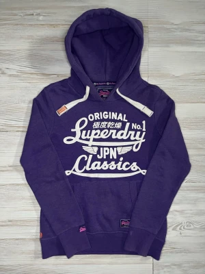 Lila Superdry hoodie med tryck - Snygg lila hoodie från Superdry med stort vitt tryck på bröstet där det står 'Superdry JPN Classics'🤩Hoodien är i fint skick och passar S🙌🏻 Hör av er vid funderingar samt snabbaffär😇