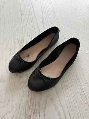 Svarta ballerinaskor med rosett - Klassiska svarta ballerinaskor med rund tå och liten rosett framtill. 
