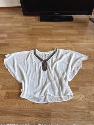 Blus Vero Moda stl XS - Säljer en elegant vit blus från Vero Moda med v-ringning och dekorativa pärlor längs halsringningen. Genomskinlig, så perfekt att ha över ett linne. ✨️ finns även i svart