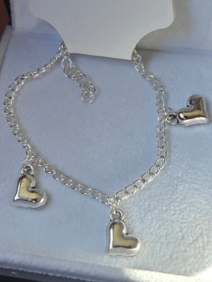 Silverfärgat armband med hjärtberlocker Rostfritt Stål  - Snyggt handgjort armband i silverfärgat rostfritt stål med tre hjärtformade berlocker. Kedjan är tunn och har ett klassiskt karbinlås. Perfekt för dig som gillar enkla men söta detaljer till din stil.