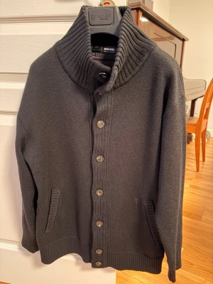 Button Cardigan Stickad - Mysig svart kofta från Woolrich med grovstickad hög krage och knappar hela vägen fram. Två fickor framtill och ribbade muddar vid ärmslut och nederkant. Perfekt för lager på lager och en clean look.