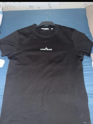 Svart Stone Island t-shirt med tryck - Säljer en svart t-shirt från Stone Island med liten logga på bröstet och stort, unikt vitt tryck med logga på ryggen. Klassisk rund hals och korta ärmar. Perfekt för dig som vill ha en stilren men ändå statement t-shirt.