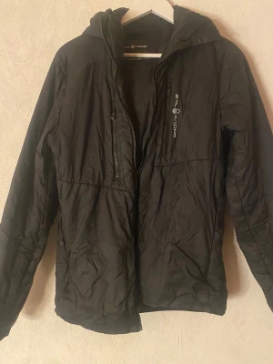 Svart jacka från Sail Racing - Säljer en svart vindjacka från Sail Racing med huva och dragkedja framtill. Jackan har två bröstfickor med dragkedja och logga på vänster sida. Lätt och smidig modell, perfekt för blåsiga dagar. Materialet är tunt och vindtätt. Säljer billigt pga att dragkedjan tyvärr inte funkar och ett hål i vänster armbåge🤍