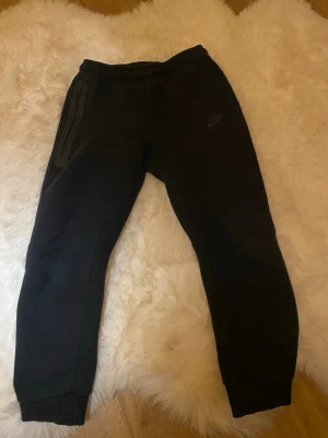 Svarta mjukisbyxor från Nike - Säljer ett par svarta mjukisbyxor från Nike med resår i midjan och muddar vid bensluten. Byxorna har en dragkedjeförsedd ficka på sidan och är tillverkade i mjukt, bekvämt material. Perfekta för chill eller träning. Om du inte är nöjd med priset så kan vi snacka🥰(köp nu tänk sen) ops! Det är large barnstorlek 