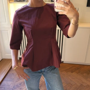 Vinröd topp med trekvartsärm - Snygg vinröd topp med trekvartsärm och figurnära passform. Toppen har rund halsringning och markerad midja som ger en feminin siluett. Perfekt att styla med jeans eller kjol för en trendig look.