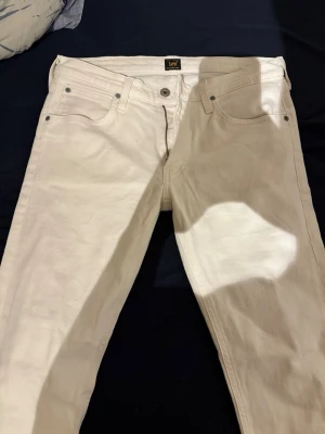 Vita raka jeans från Lee - Snygga vita jeans från Lee med klassisk femficksmodell och raka ben. Jeansen har silverfärgade nitar och knapp, samt Lee-logga i midjan. Tillverkade i ett slitstarkt bomullstyg som känns bekvämt och passar till många olika stilar.