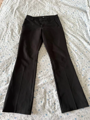Svarta kostymbyxor bootcut - Snygga svarta kostymbyxor från BikBok, med bootcut passform och lågmidjade. Byxorna har fickor i sidorna och hällor för skärp. Perfekta för en clean och stilren look. Materialet känns slätt och klassiskt.