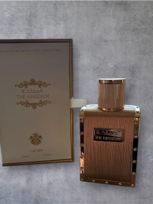 Lattafa The Kingdom Eau de Parfum - Lyxig parfym från Lattafa, The Kingdom, i en elegant guldfärgad flaska med räfflad design och dekorativa nitar. Flaskan har en exklusiv känsla och levereras i en matchande guldfärgad box. Doften är orientalisk och exklusiv.