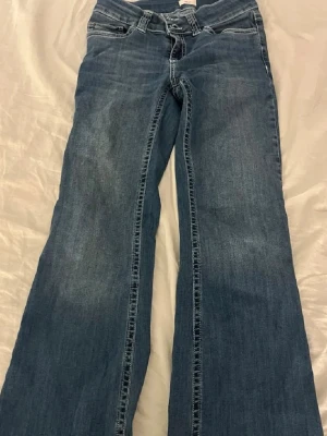 Blå bootcut jeans med broderade fickor - (Nersydda att passa mig som är 160 )Säljer ett par blå bootcut jeans med snygga broderade detaljer på bakfickorna. Jeansen har klassisk femficksmodell, normal midja och är tillverkade i denim. Perfekta för dig som gillar en avslappnad men trendig stil.