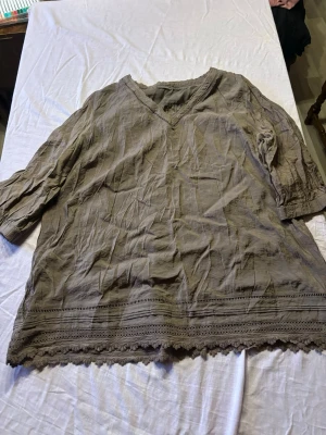 Beige blus med spetsdetaljer - Luftig beige blus med v-ringning och trekvartsärmar. Blusen har fina spetsdetaljer längs nederkanten och vid halsen, samt ett lätt skrynklat tyg som ger en avslappnad look. Perfekt till jeans eller kjol för en chill stil.