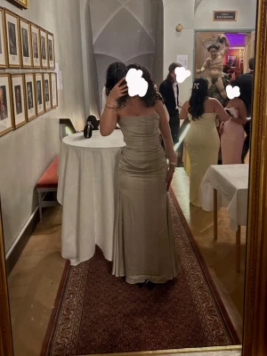 Champagnefärgad/ljus grön axelbandslös långklänning - Elegant axelbandslös långklänning i champagnefärg/ ljus grön med figurnära passform och lätt utsvängd nederdel. Klänningen har en slät yta och markerad midja, vilket ger en stilren och lyxig look. Perfekt för speciella tillfällen.