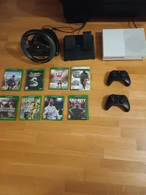 Xbox One vit med ratt, pedaler och spel - Säljer en vit Xbox One med två svarta handkontroller, ratt och pedalset för racing. Xboxen är i bra skick den funkar. Köparen får med alla sladdar som hdmi och mer. Ratten och pedalerna glappar lite och behöver några fler sugproppar men den funkar om man orkar fixa. En av handkontrollerna har lite stickdrift men funkar ändå helt okej har också bytt joysticks. Alla spel funkar till xboxen. Skriv för mer information. Säljer eftersom att jag har fått ett PC👍.  Pris kan diskuteras.