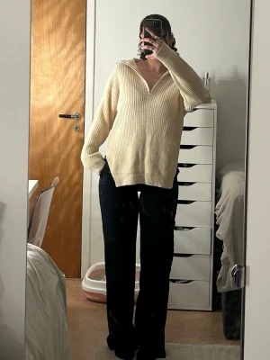 Beige ribbad tröja med dragkedja - Säljer en beige ribbad tröja med krage och halv dragkedja framtill. Tröjan har en avslappnad passform och långa ärmar, perfekt för en chill och stilren look. Passar till både jeans och byxor för en enkel vardagsstil.   Säljer en beige stickad tröja med djup v-ringning och avslappnad passform. Den har även slits på bägge sidorna!