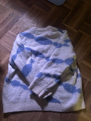 Vit stickad tröja med blått mönster - Mysig stickad tröja i vitt med stora blå ovala mönster längs hela tröjan. Superfin nu till våren och sommarkvällar, tröjan är knappt använd 💙💙Storlek L, men sitter mer som M