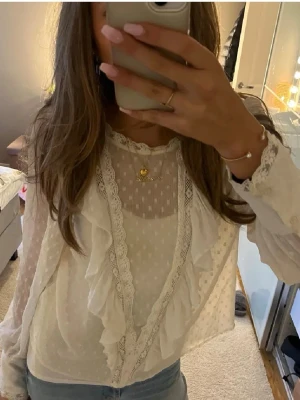 Vit romantisk blus med spetsdetaljer - vit blus med volanger och spetsdetaljer. Blusen har transparent tyg med prickigt mönster, rund halsringning och långa ärmar med spetskant. Har ett linne under på bilden, använd endast 2 gånger.