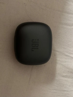 Svarta trådlösa in-ear hörlurar JBL - Snygga svarta trådlösa in-ear hörlurar från JBL med laddningsetui. Hörlurarna har en stilren, matt finish och laddas smidigt i det kompakta fodralet. Perfekta för musik, poddar och samtal på språng.