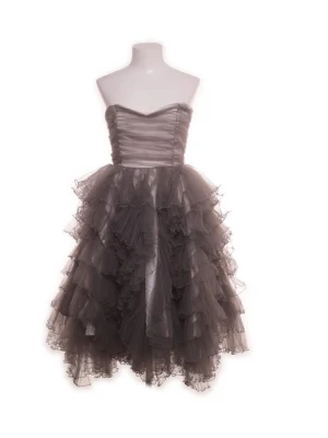 Grå volangklänning Ida Sjöstedt - Supersnygg cocktailklänning från Ida Sjöstedt med flera lager volanger och axelbandslös design. Klänningen har ett omlottliknande liv och är tillverkad i ett glansigt, tunt material som ger en lyxig känsla. Perfekt för dig som vill sticka ut med en dramatisk look. Köpt på second hand för 700kr