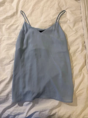 Ljusblå linneblus från Lindex - Säljer en ljusblå linnetopp från Lindex med tunna axelband och v-ringad hals. Toppen har en enkel och stilren design som passar perfekt till jeans eller kjol. Materialet känns lätt och svalt, perfekt för varma dagar. Aldrig använd av mig men köpt second hand i bra skick💗💗