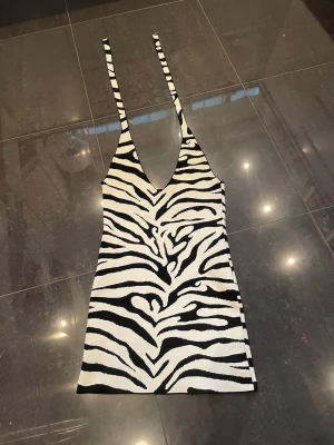 Zebramönstrad kort klänning Gina Tricot - Säljer en zebramönstrad kort klänning från Gina Tricot. Klänningen är svartvit med djup v-ringning och smala axelband. Materialet är stickat och stretchigt, vilket ger en bekväm passform. Perfekt för dig som vill sticka ut med ett trendigt mönster.