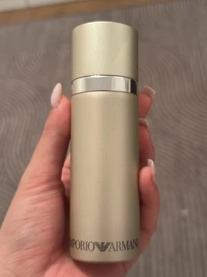 Emporio Armani parfym beige metall - Snygg parfym från Emporio Armani i en stilren beige metallflaska med silverdetaljer. Flaskan har en rund, cylinderformad design och loggan är tryckt längst ner. Perfekt för dig som gillar exklusiva dofter och elegant design. Lite mer än halva full. 