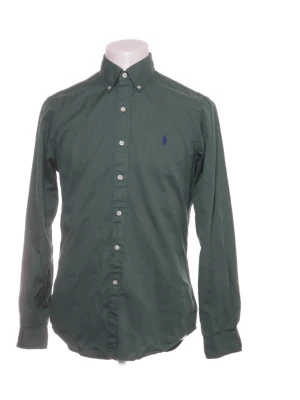 Grön skjorta från Ralph Lauren - Mörkgrön skjorta från Ralph Lauren med klassisk button-down krage och broderad logga på bröstet. Skjortan har långa ärmar, vita knappar framtill och är tillverkad i mjuk bomull. Perfekt för en stilren och avslappnad look.