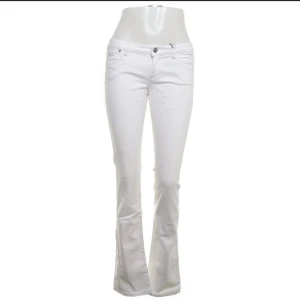 Vita bootcut jeans från Guess - Snygga vita jeans från Guess med bootcut-passform. Klassisk femficksmodell med låg midja och diskreta broderade detaljer på bakfickan. Tillverkade i mjuk bomull med lite stretch för extra komfort. Perfekta för dig som vill ha en fräsch och stilren look. Egenklippta slitsar på utsidan av benen för mer bootcut effekt